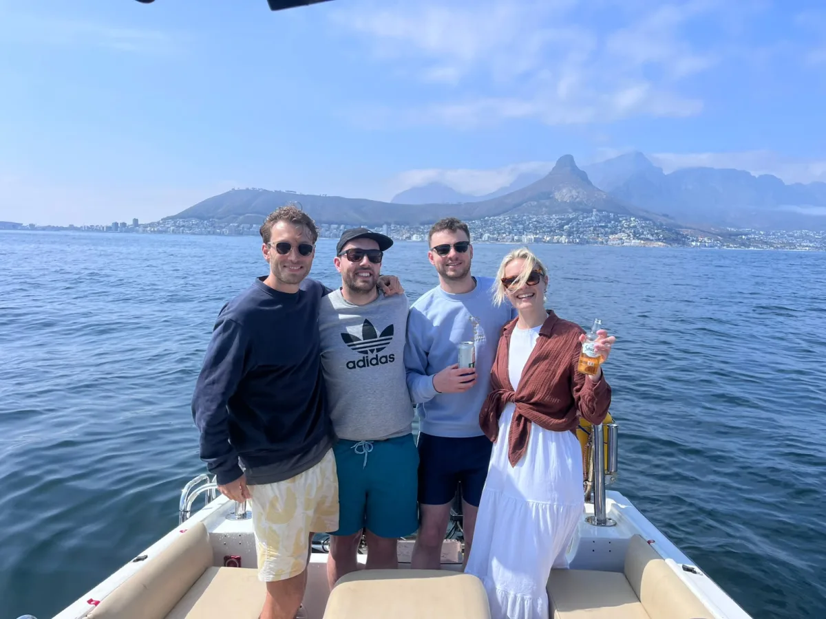 Guests toasting with drinks on board, with Lion's Head and the Cape Town coastline behind